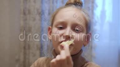 快乐少年女孩在家厨房吃薯片。 一个快乐的少女在家里吃脆脆的薯片